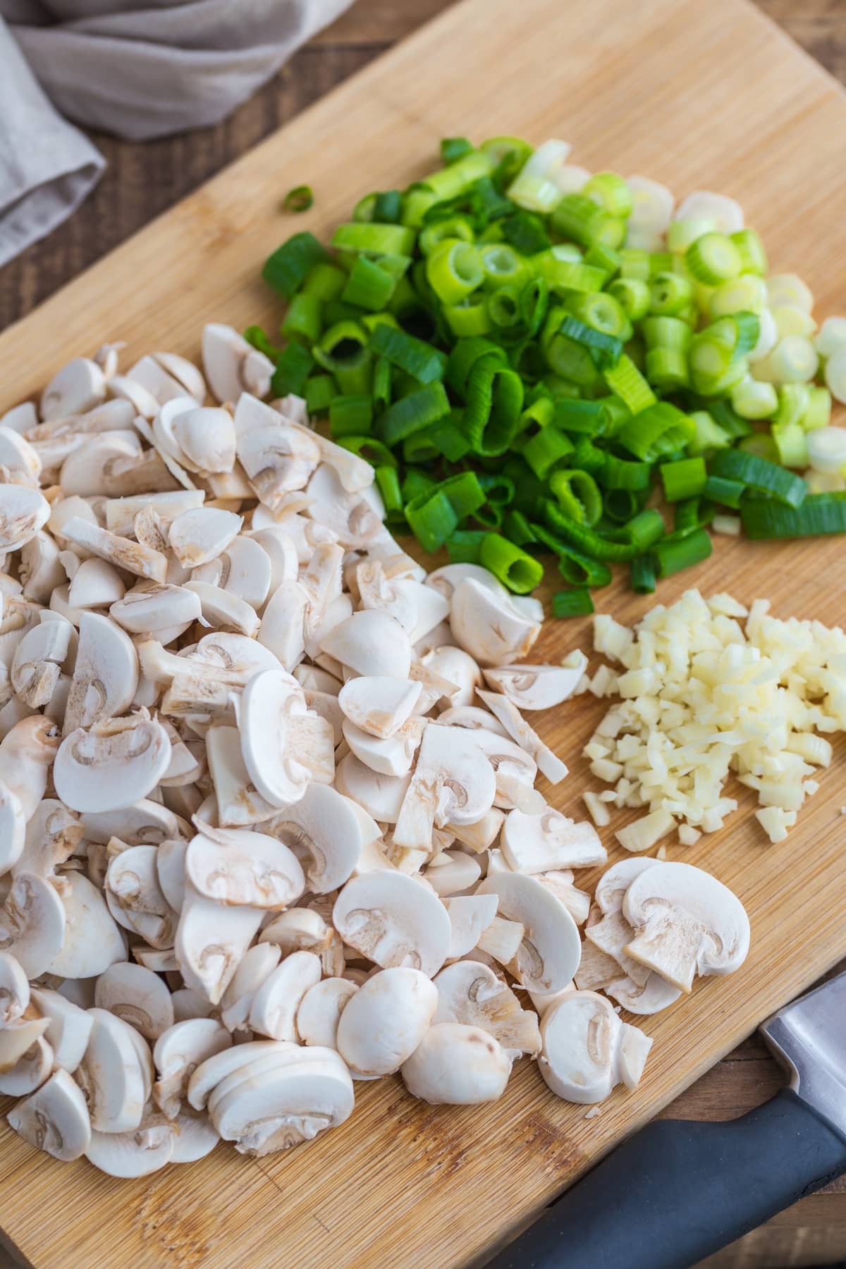 Chopped garlic, mushrooms and spring onion on a cutting board.