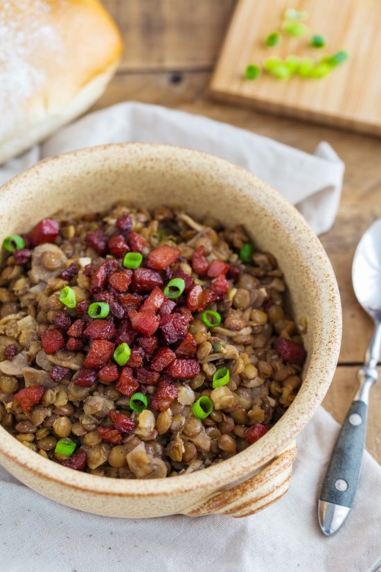 Crispy bacon and fresh spring onion topping a portion of lentil stew.