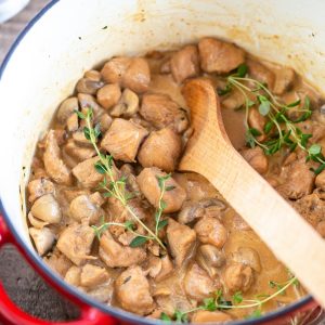 Cream cheese chicken and mushrooms stew in a red Dutch oven pot.