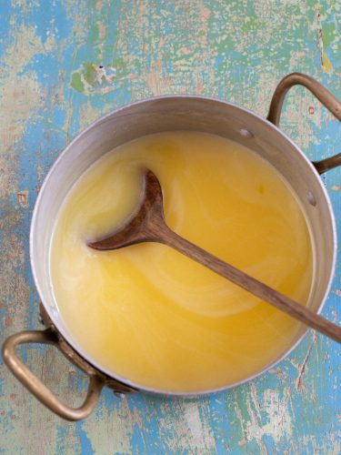 Lemon curd in a pot, whisked with a wooden spoon.