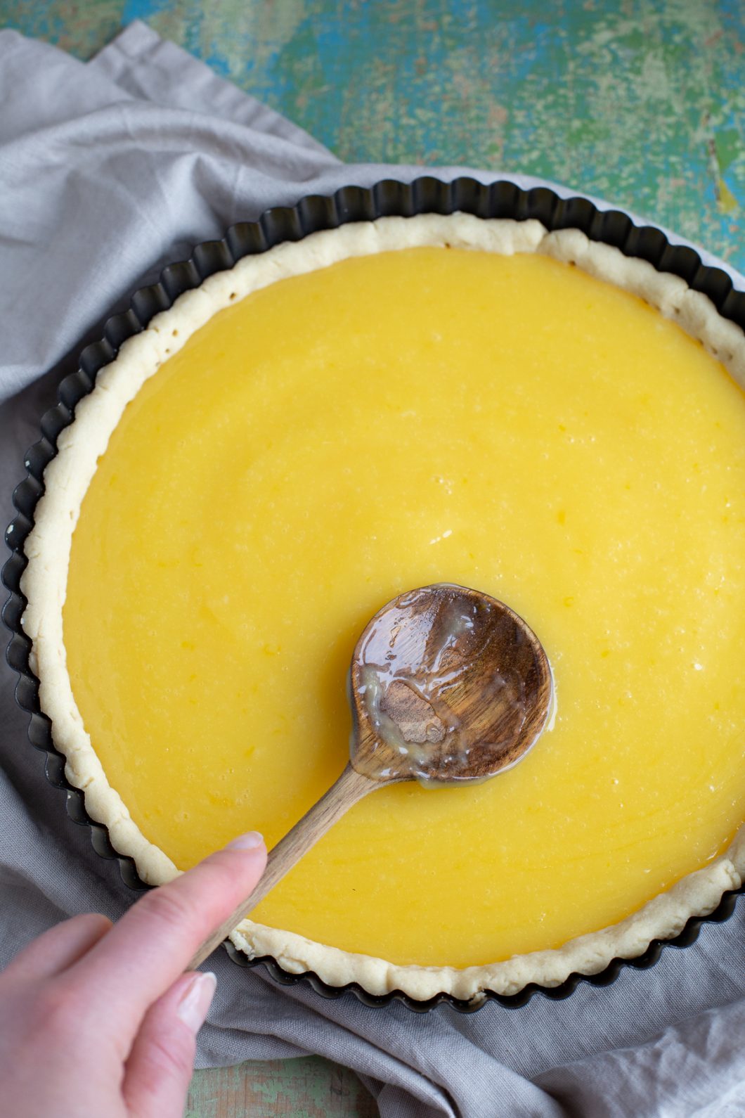Spreading lemon curd over shrtcrust shell with a wooden spoon.