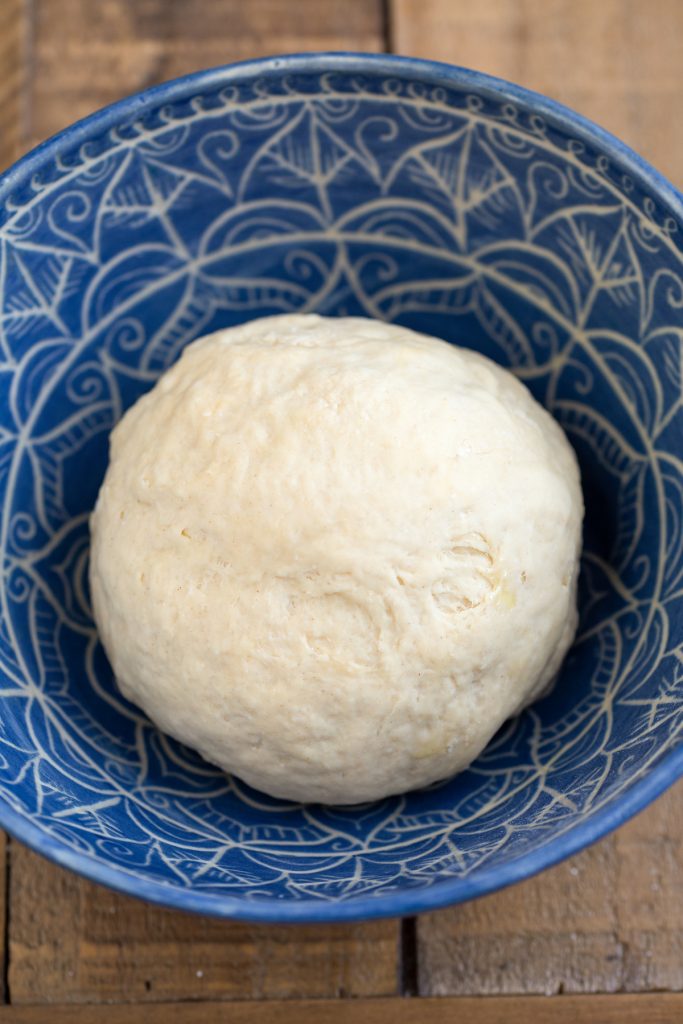 Pizza dough ball in a blue bowl.