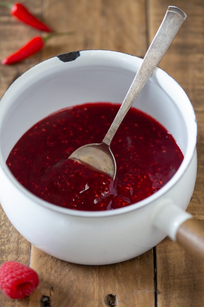 Raspberry chili coulis in a white enamel pot.