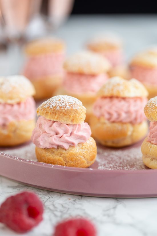 Raspberry cream puffs on a pink plate.
