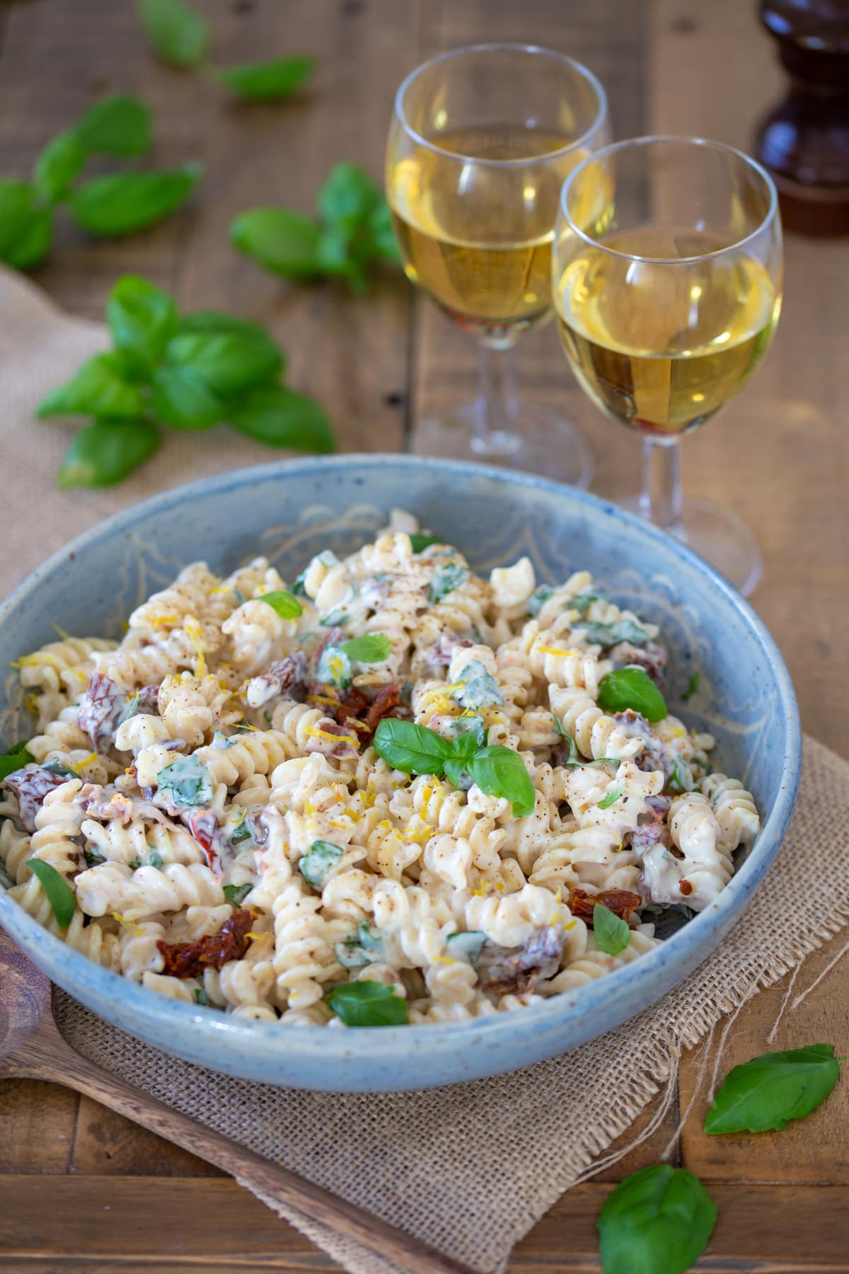 This pasta salad in a bowl, with 2 glasses of wine aside.