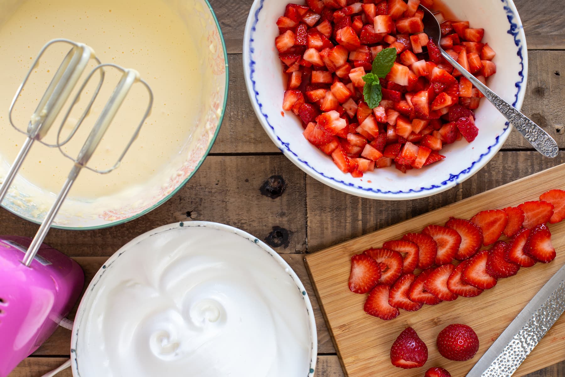 One bowl with whipped egg whites, one with whipped yolks and mascarpone, and a bowl with diced strawberries.
