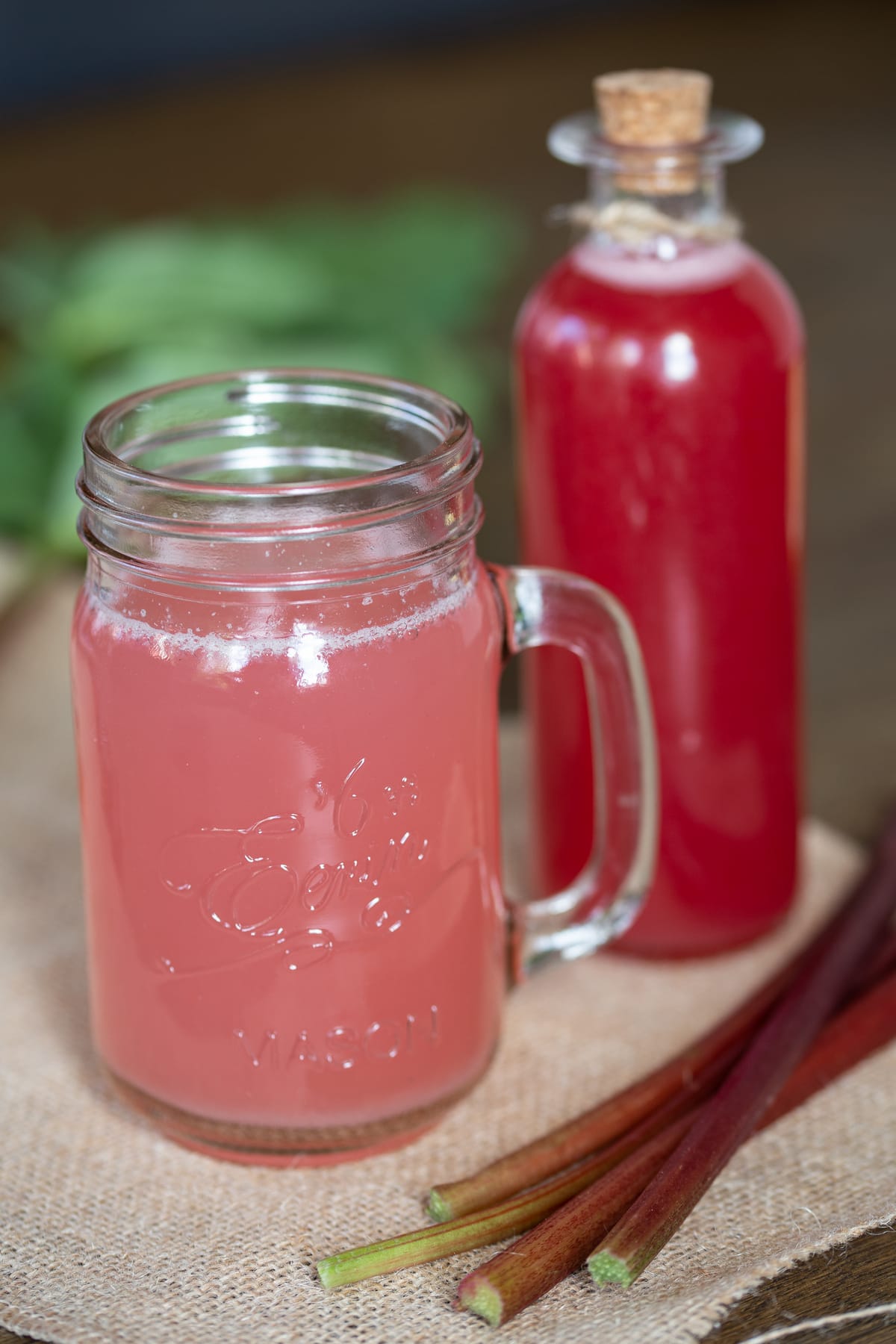 A glass of rhubarb syrup drink and the bottle of concentrate behind.