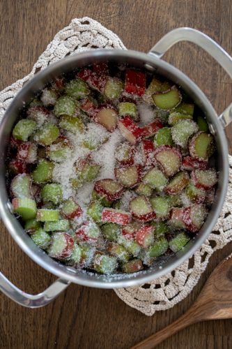 Chopped rhubarb tossed with sugar in a stainless steel pot.
