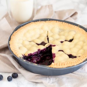 Blueberry pie, sliced. A glass of milk in the background.