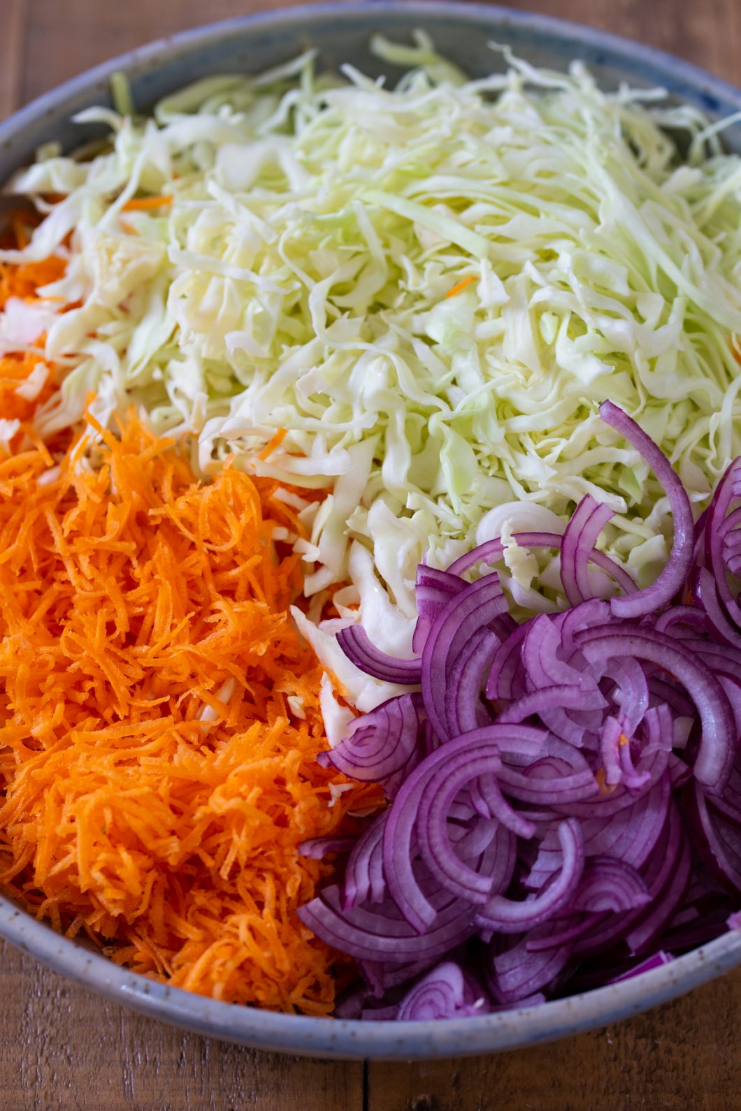 Thinly sliced carrot, white cabbage and onion together in a bowl.