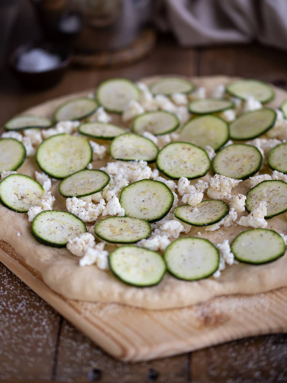 Unbaked pizza bianca topped with fresh zucchini and feta.