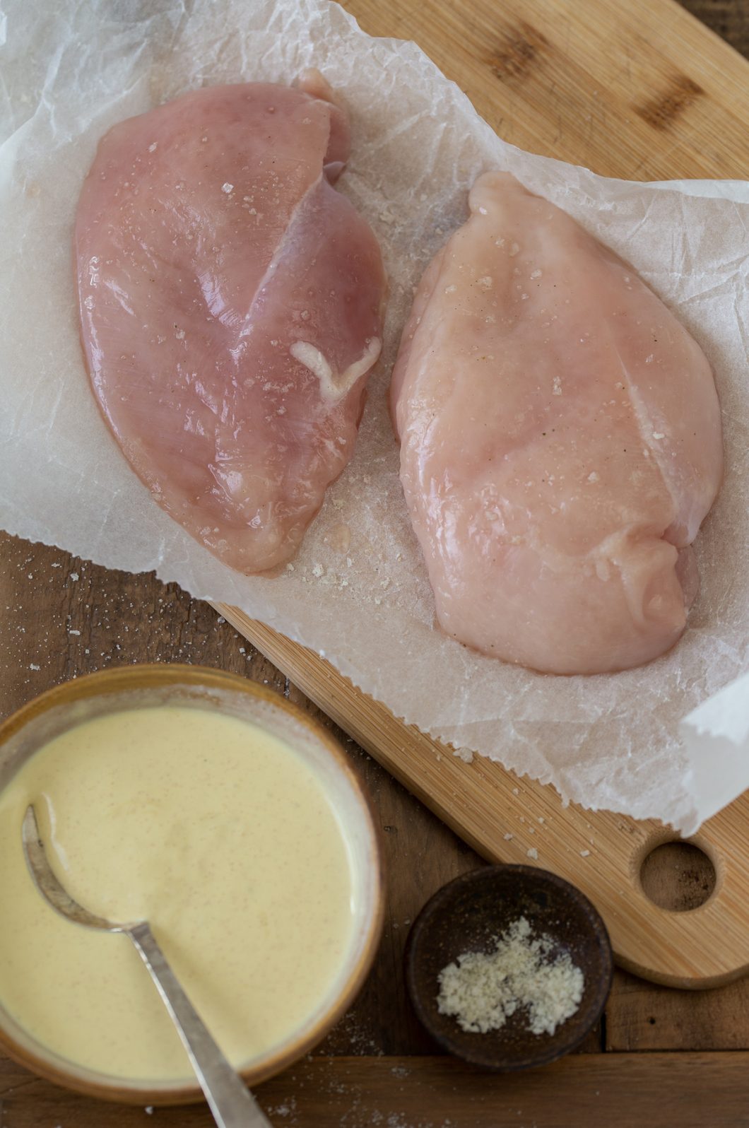 Chicken breasts on a cutting board, a bowl with the condiment on the side.