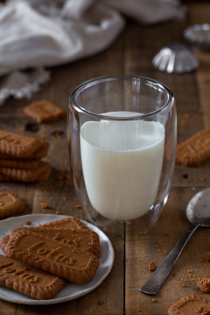 A glass of milk with biscuits all around.