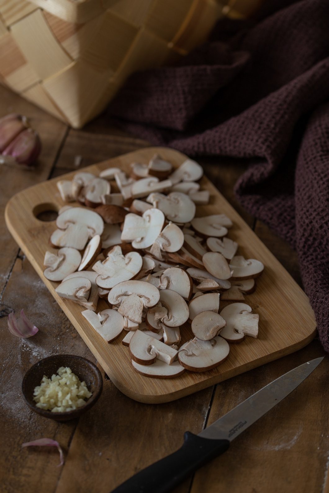 Baby bella mushrooms sliced on a wooden cutting board.