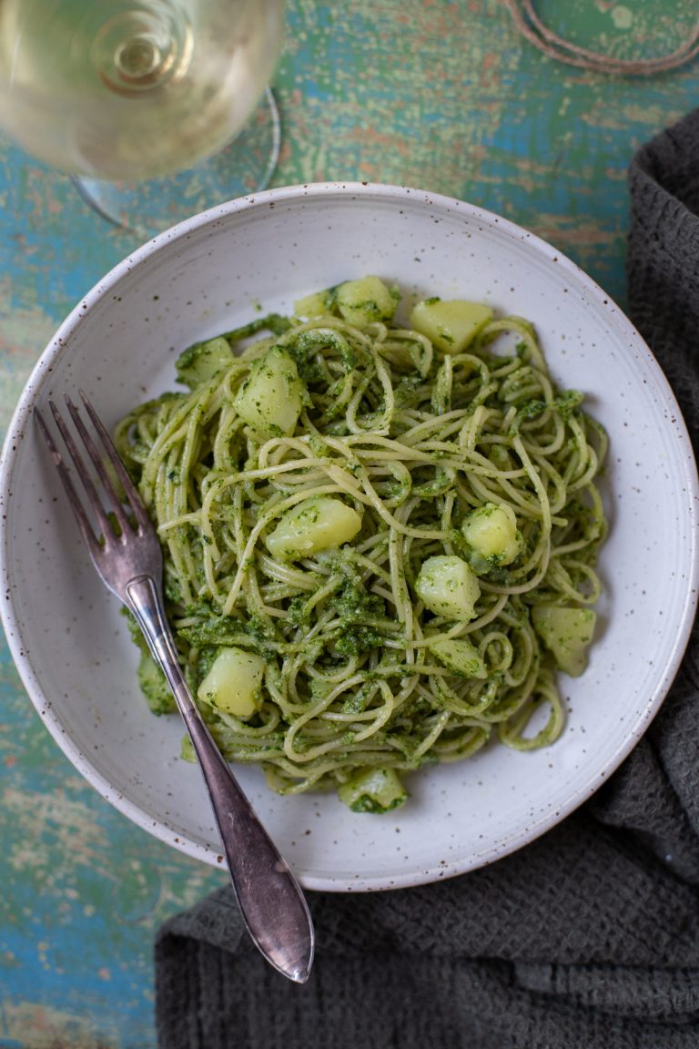 A portion of pesto pasta with potatoes in a white bowl.