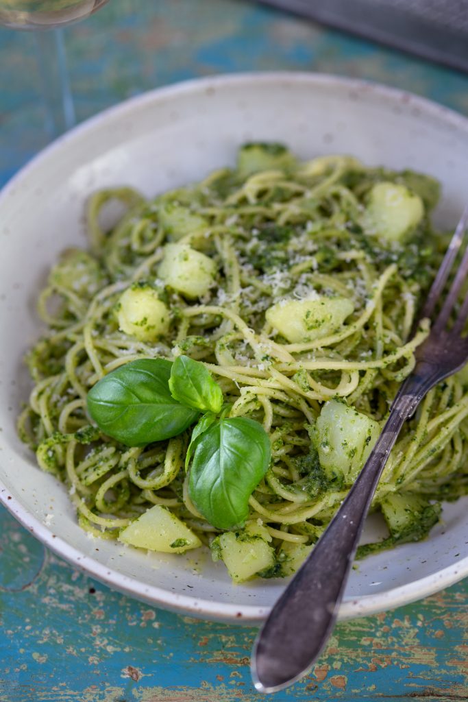 A portion of pesto pasta with potatoes in a white bowl.