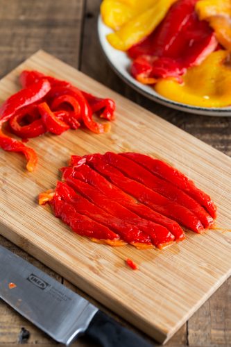 Slicing roasted pepper on a wooden cutting board.