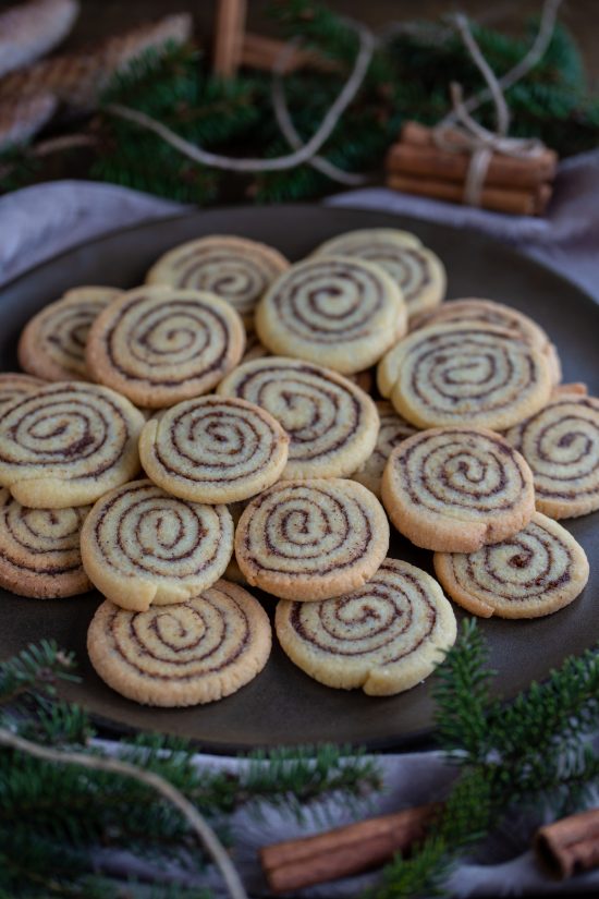 Kanelbulle cookies on a brown plate with pine decorations.
