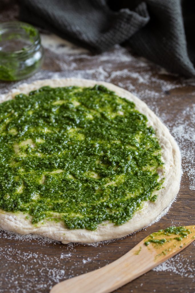 Spreading pesto on pizza.