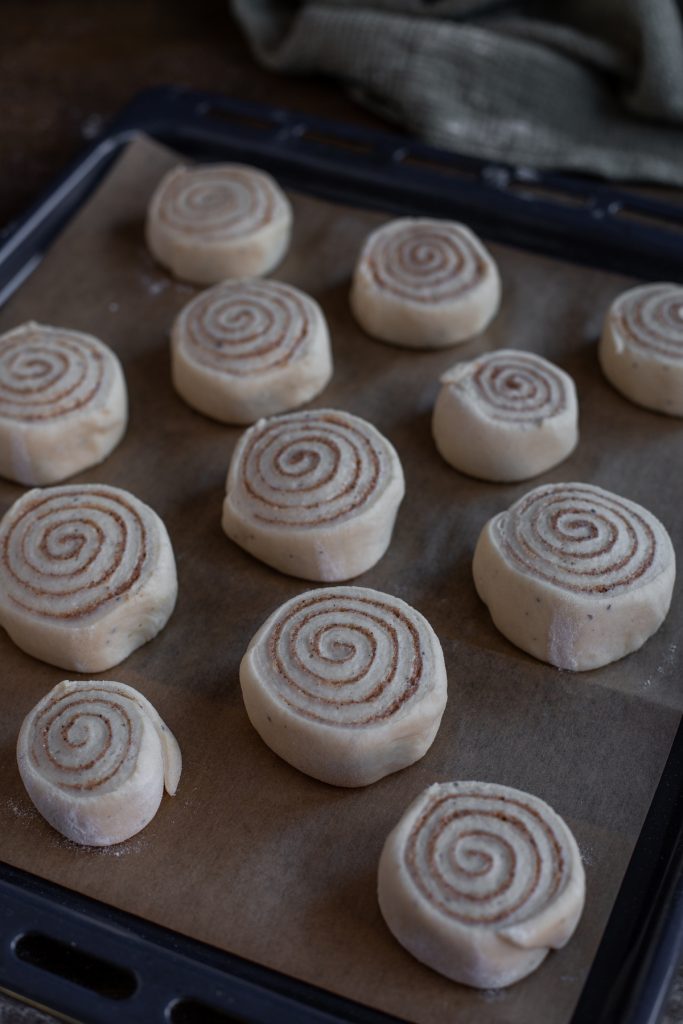 Cinnamon rolls proofing on an oven tray.