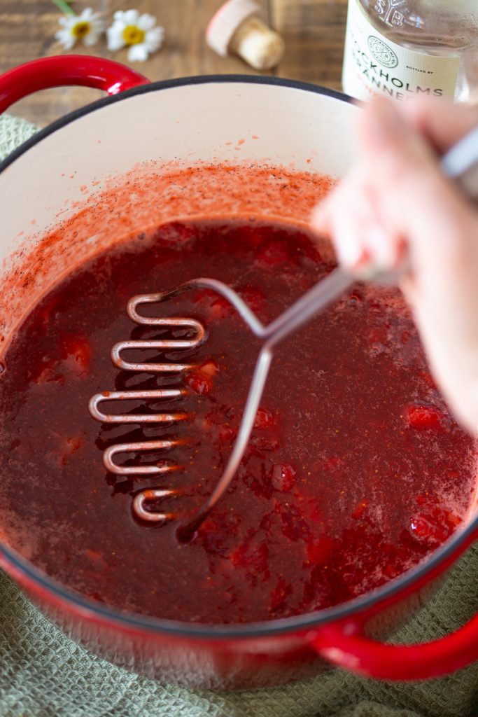 Mashing strawberries in a pot to make strawberry jam.