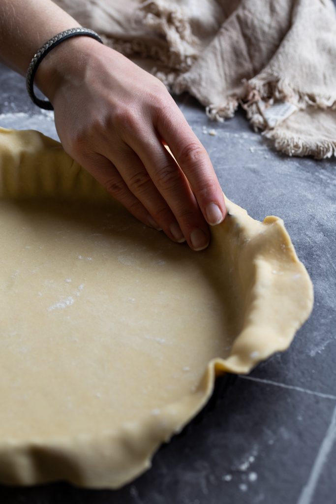 Hand pressing shortcrust dough onto pie tin.