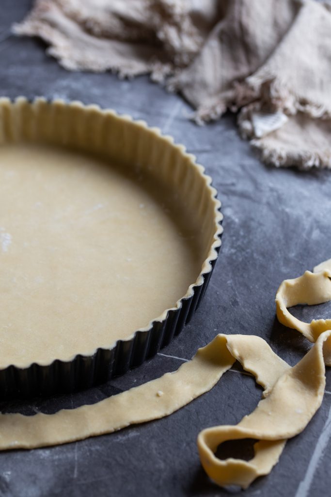 Shortcrust pastry dough pressed onto baking tin with leftover dough by the side.