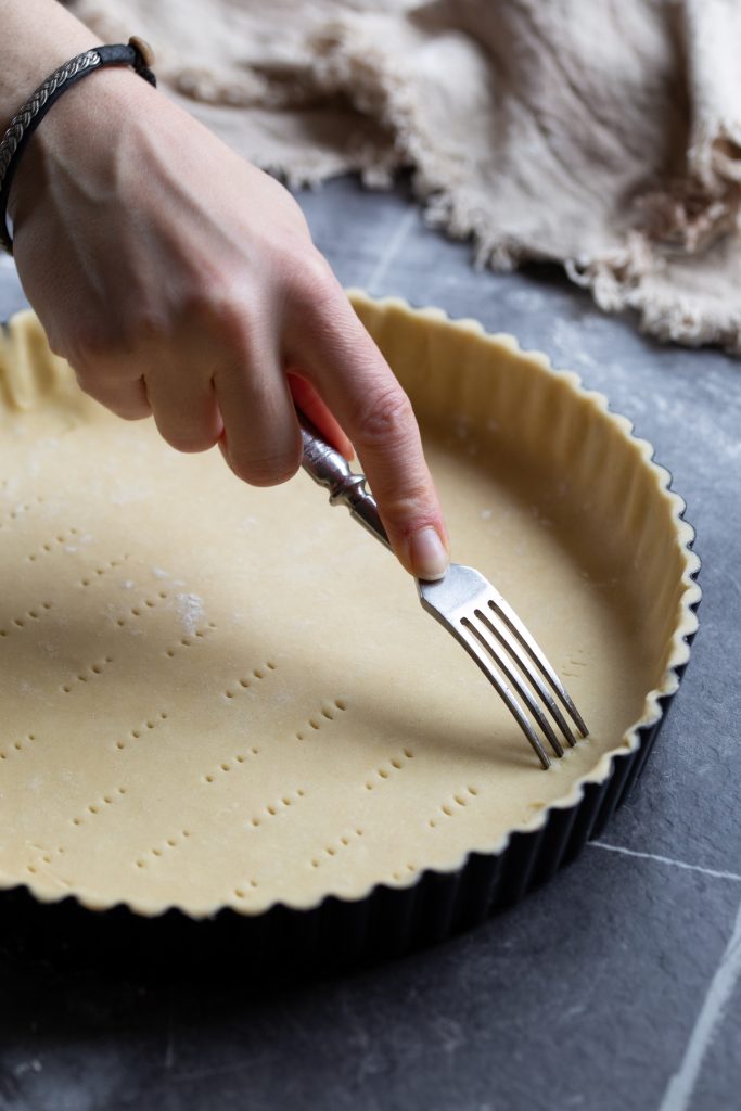 Hand pricking bottom of pie dough with a fork.