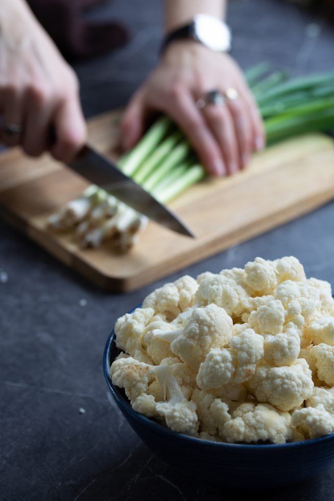 Cauliflower florets and hands chopping spring onion.