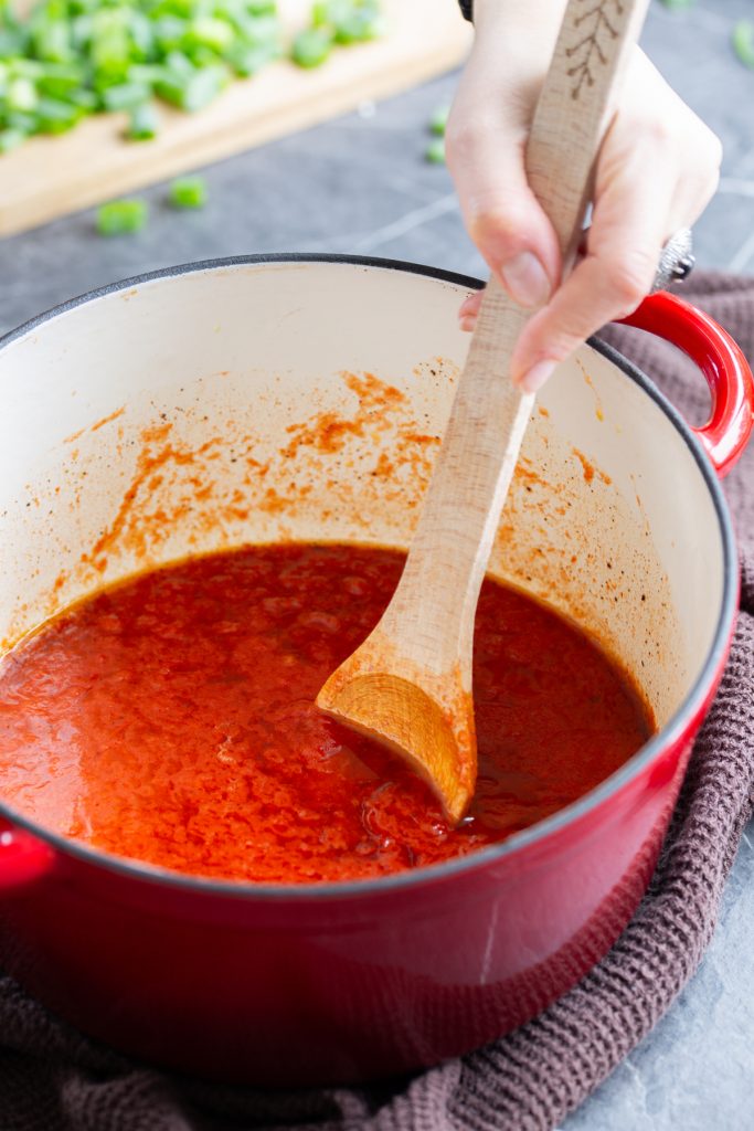 Wooden spoon stirring tomato sauce.