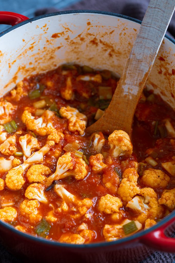 Cauliflower florets in a pot of tomato sauce.