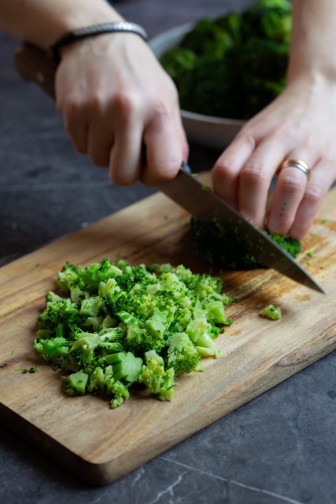 Hands chopping broccoli an wooden cutting board.