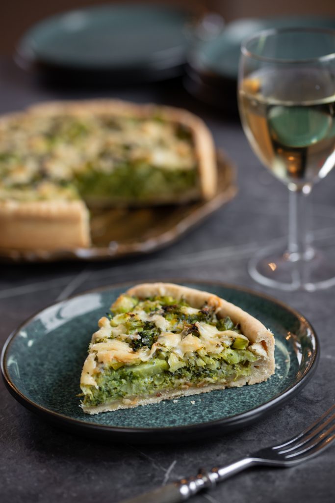 Sliced of broccoli cheese pie, rest of pie and glass of white wine in the background.