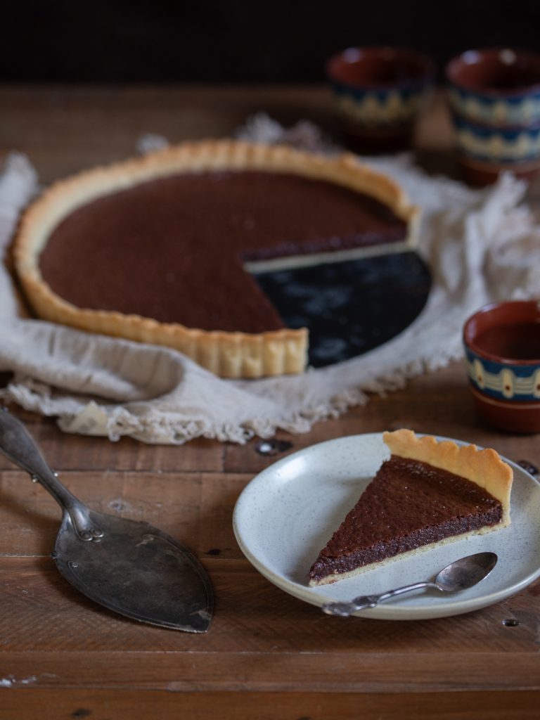 A slice of chocolate tart in the front, rest of pie in the back.