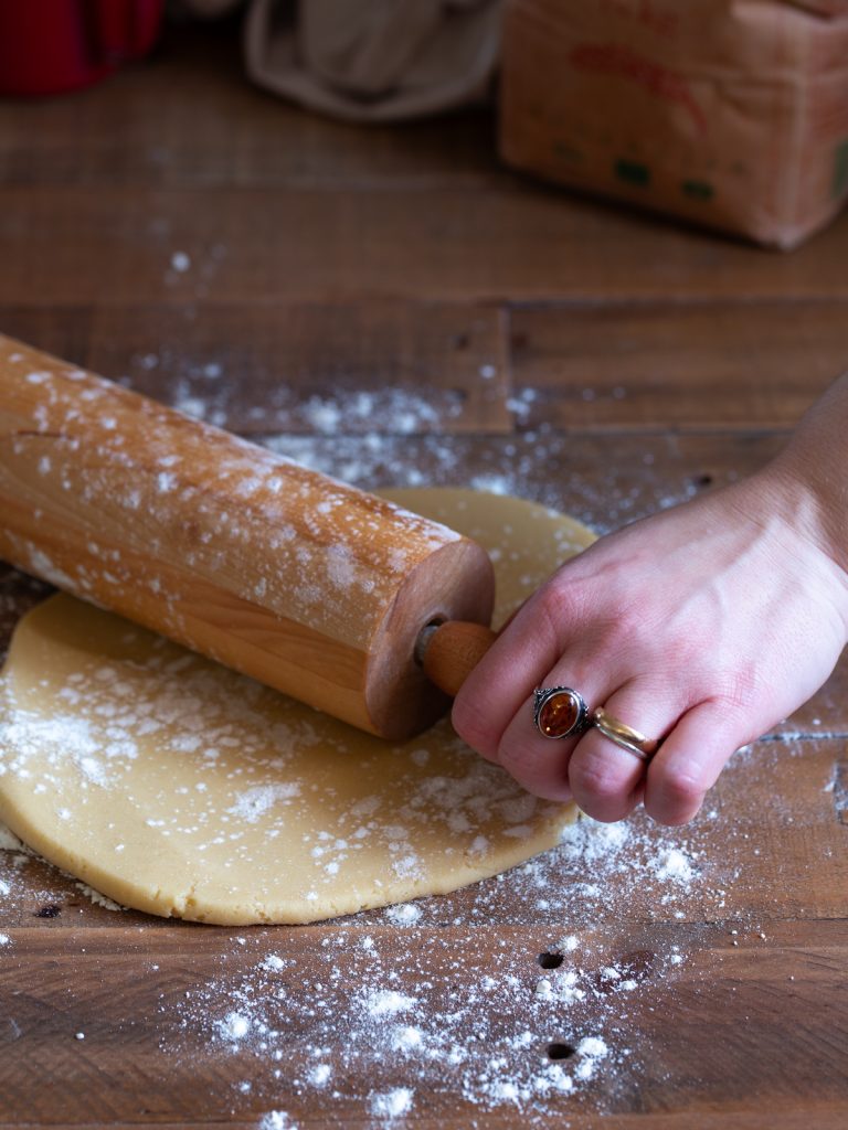 Hand with rings using a rolling pin to flatten dough.