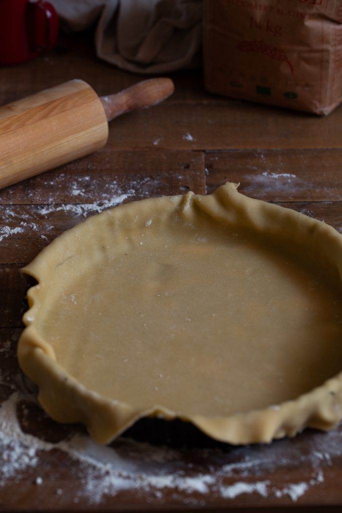 Pasta frolla being fitted inside a tart pan.
