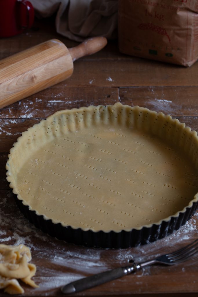 A tart pan filled with sweet shortcrust pastry, poked with a fork to not inflate during baking.