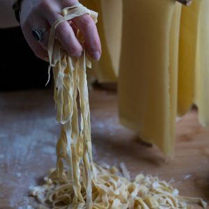 A hand with a black ring lifting fresh fettuccine pasta.