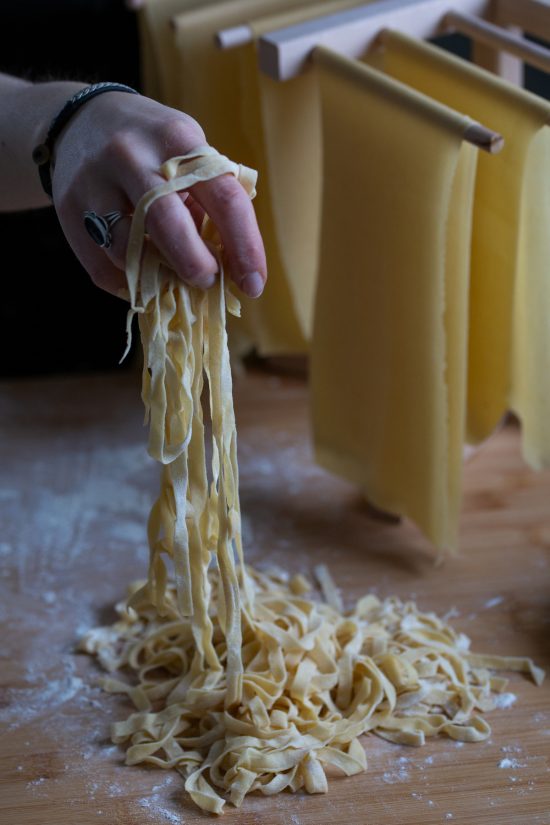 A hand with a black ring lifting fresh fettuccine pasta.