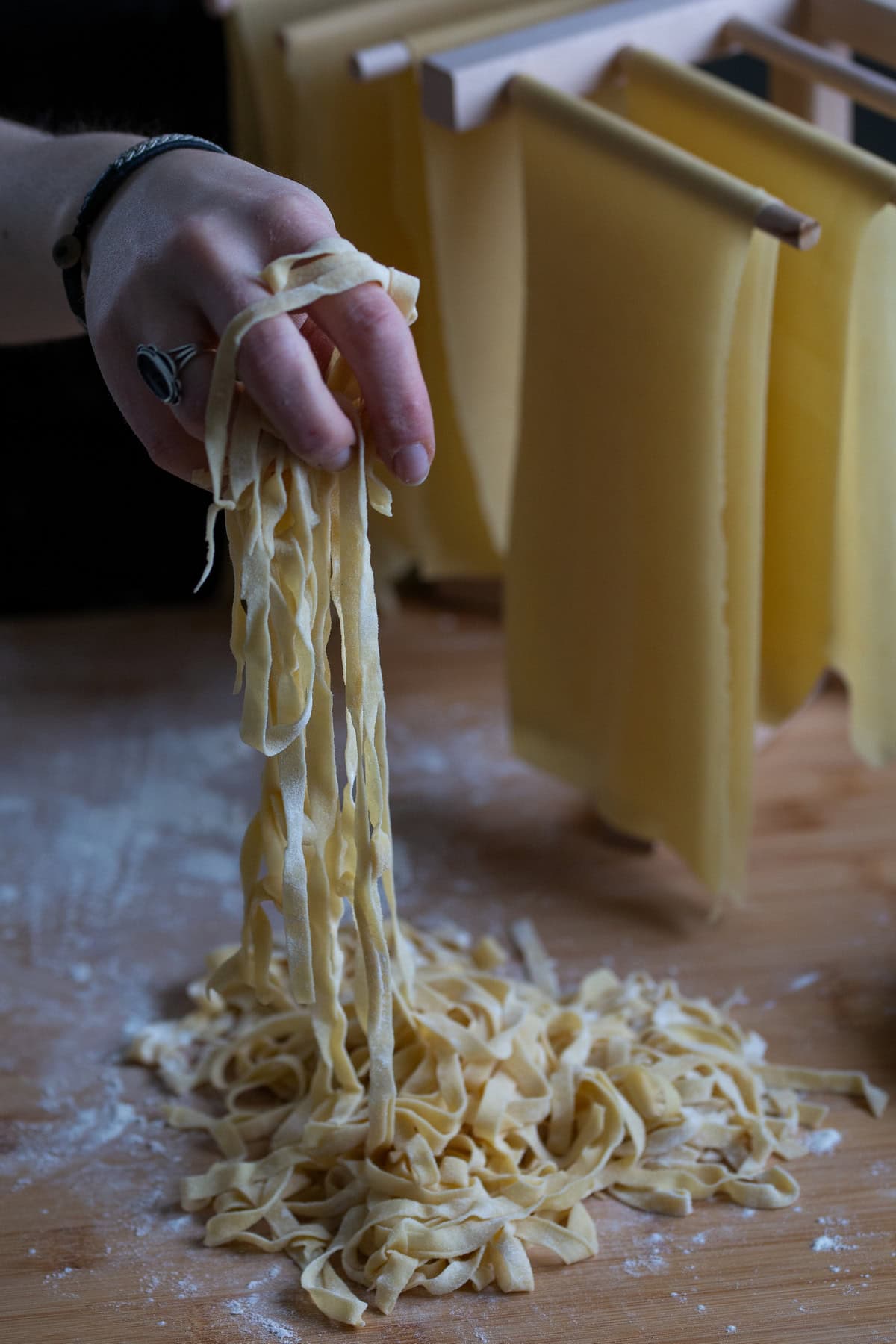A hand with a black ring lifting fresh fettuccine pasta.
