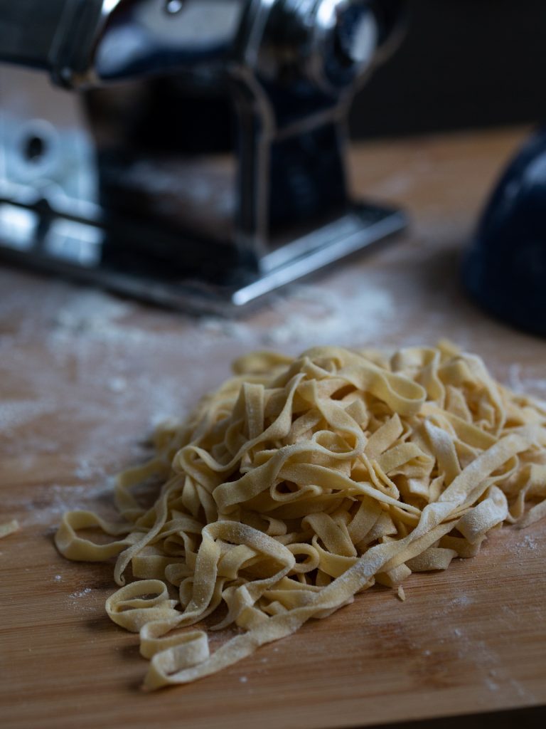 A batch of fresh fettuccine in front of a pasta machine in the background.