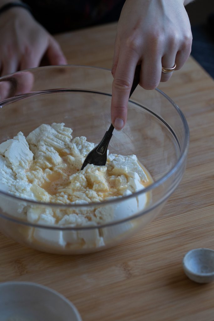 Hand working ricotta and egg mixture with a fork.