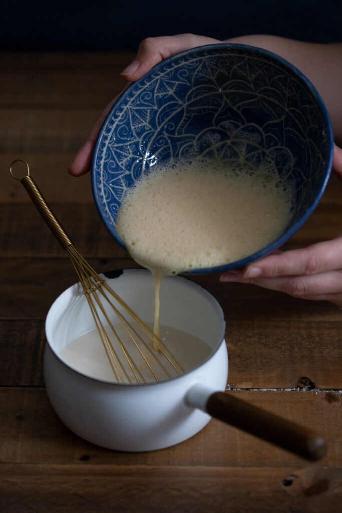 Pouring beaten egg mixture into pot with milk.