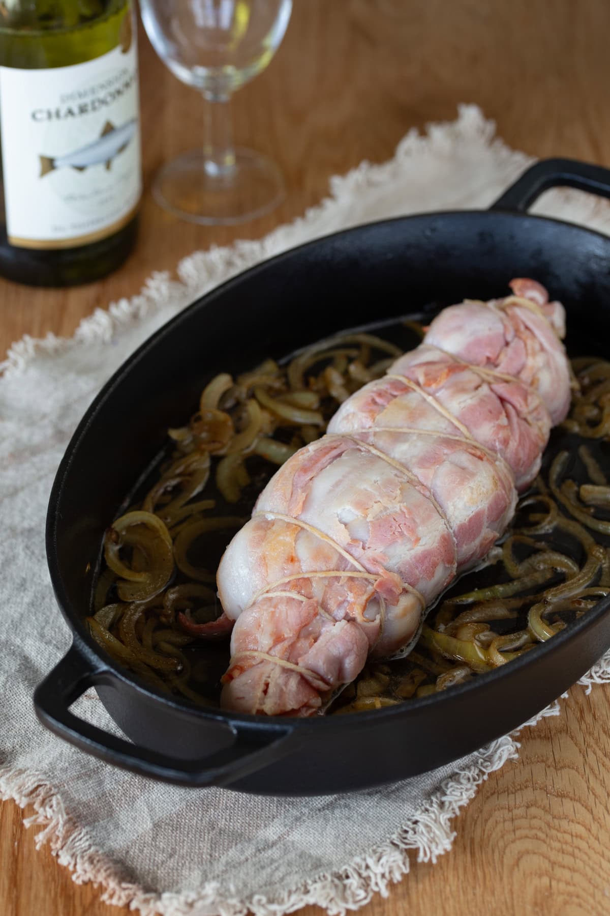 Bacon wrapped turkey breast with onions and white wine in cast iron casserole dish.