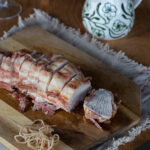 Bacon wrapped turkey breast roast sliced on cutting board.