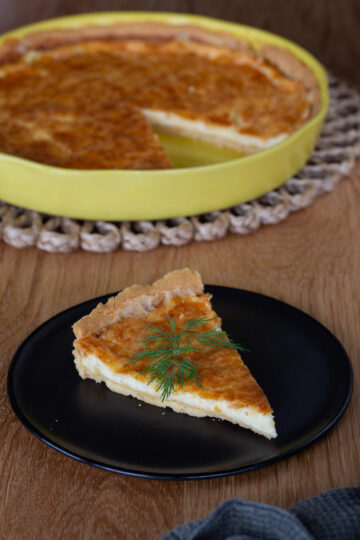 A slice of Västerbottenpaj, rest of pie in the background.