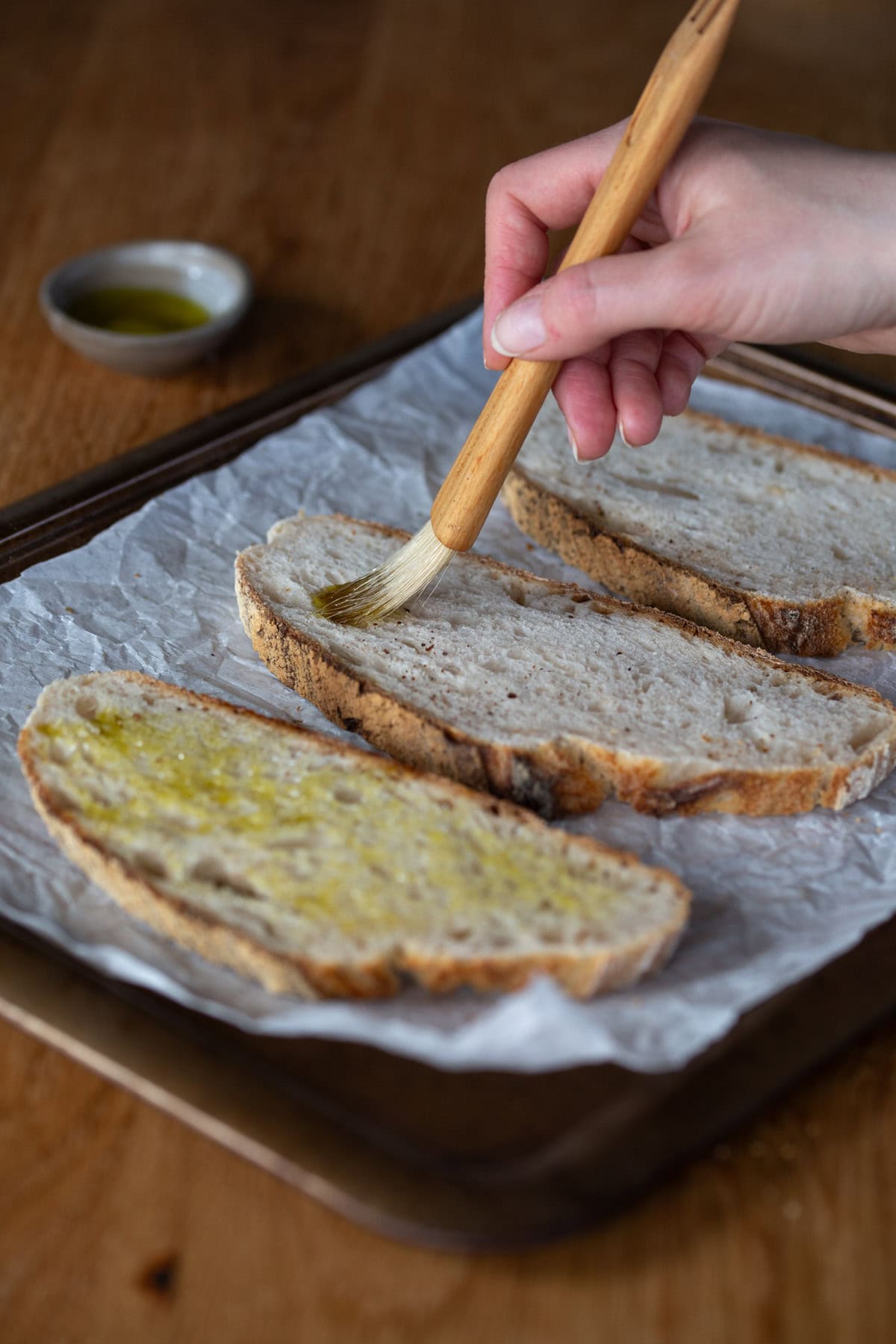 Hand brushing olive oil on bread slice with a pastry brush.