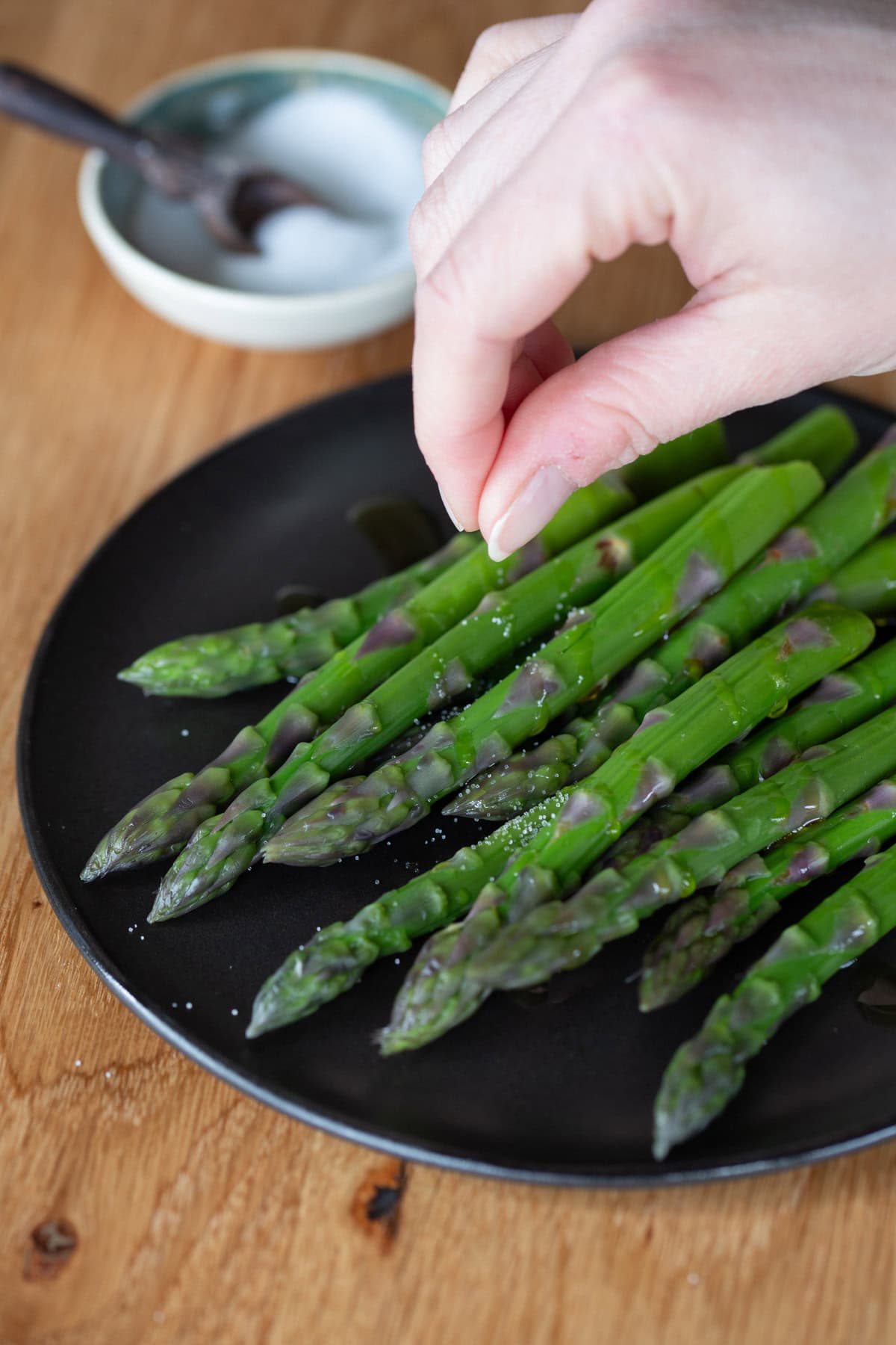 Hand sprinkling salt over cooked asparagus.