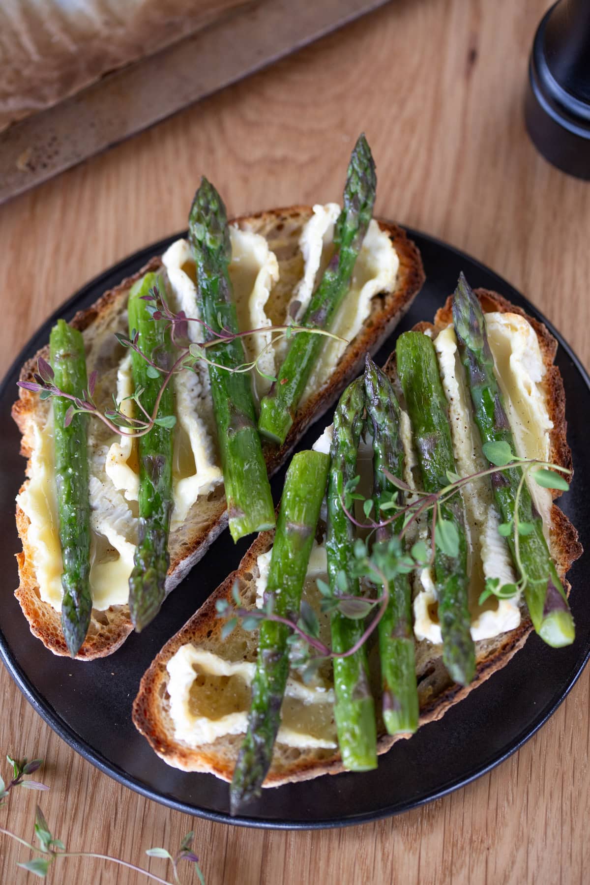 Two slices of asparagus camembert bruschetta on black plate.