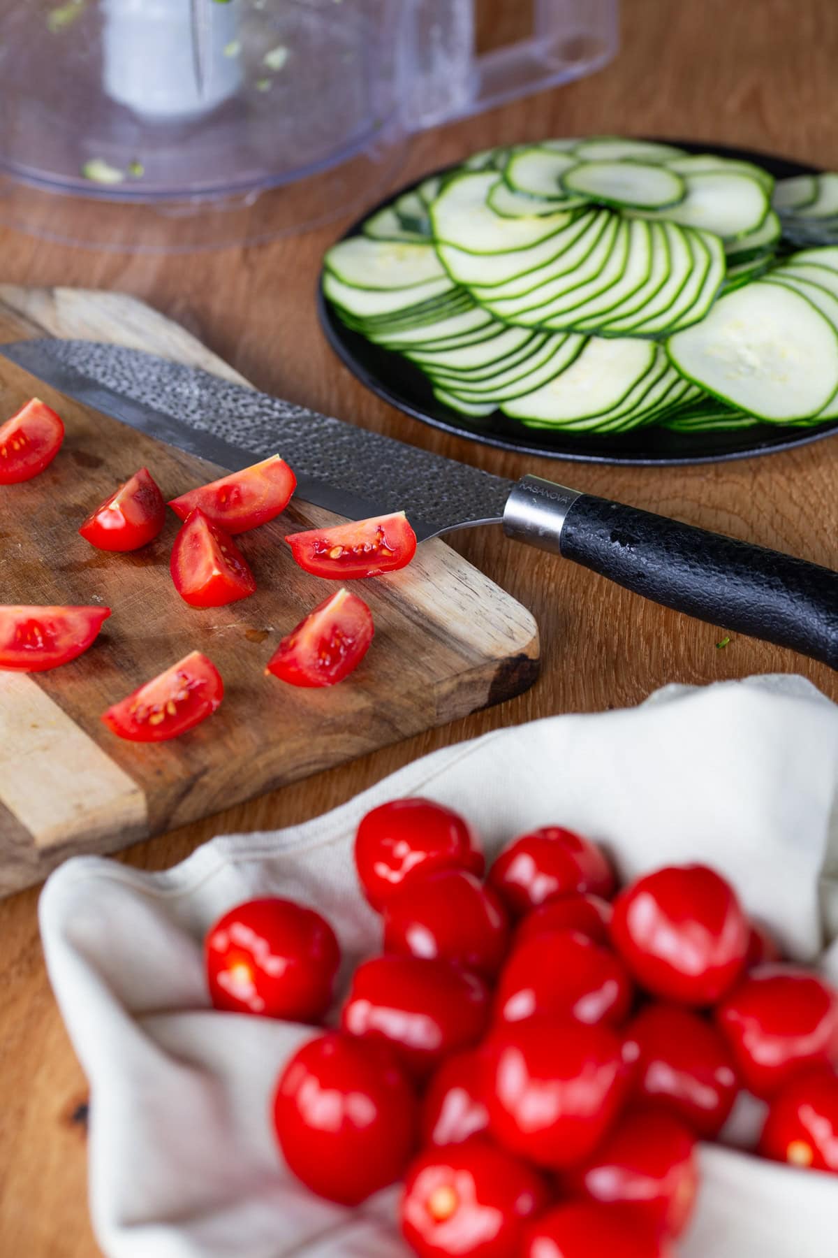 Cutting cherry tomatoes on a wooden board, sliced zucchini in the background.